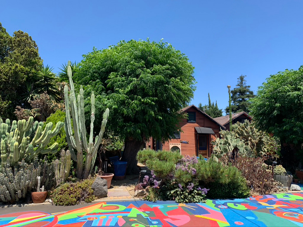 The back lot of St Elmo Village. There are trees and a colorful mural on the ground with a on story house is the background